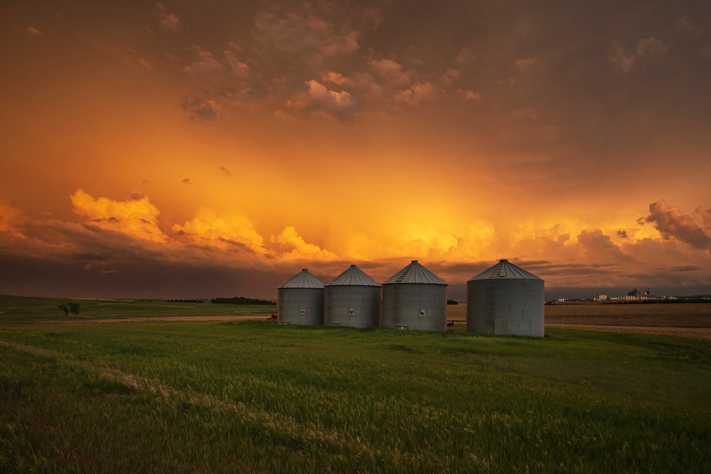 Sunset with dramatic storm clouds over four metal grain silos in a green farm field, Storm Chasing, Weather, Environmental, Winner, South Dakota, USA.