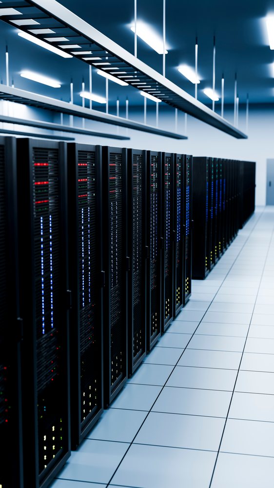 Rows of server racks with illuminated status lights inside a data center technology room with cable trays overhead and tiled floor.