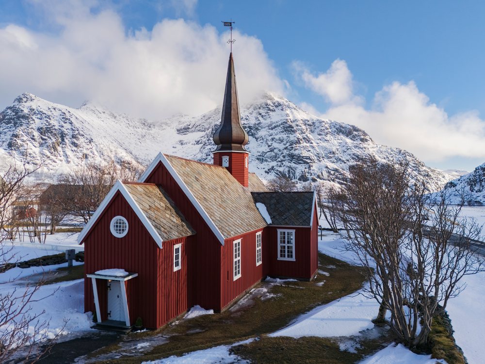 Flakstad Church is a red cruciform timber church with an onion-domed steeple near Ramsberg Mountains in winter, Landscape, Norway.