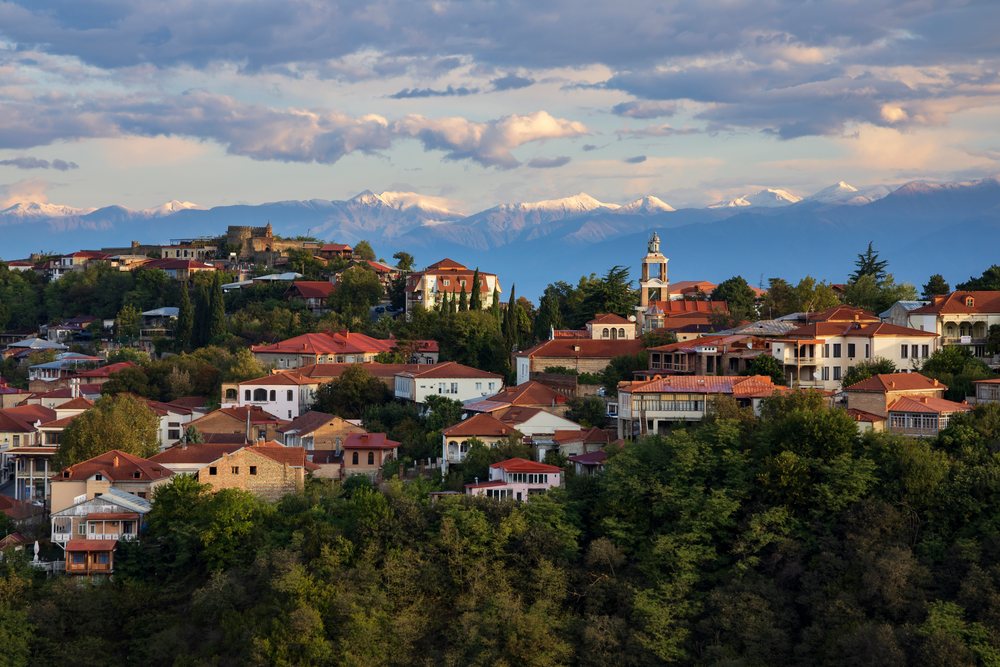 The hilltop town of Sighnaghi with red rooftops and dense trees at Sunrise, backed by snow-capped Caucasus Mountains, Georgia.