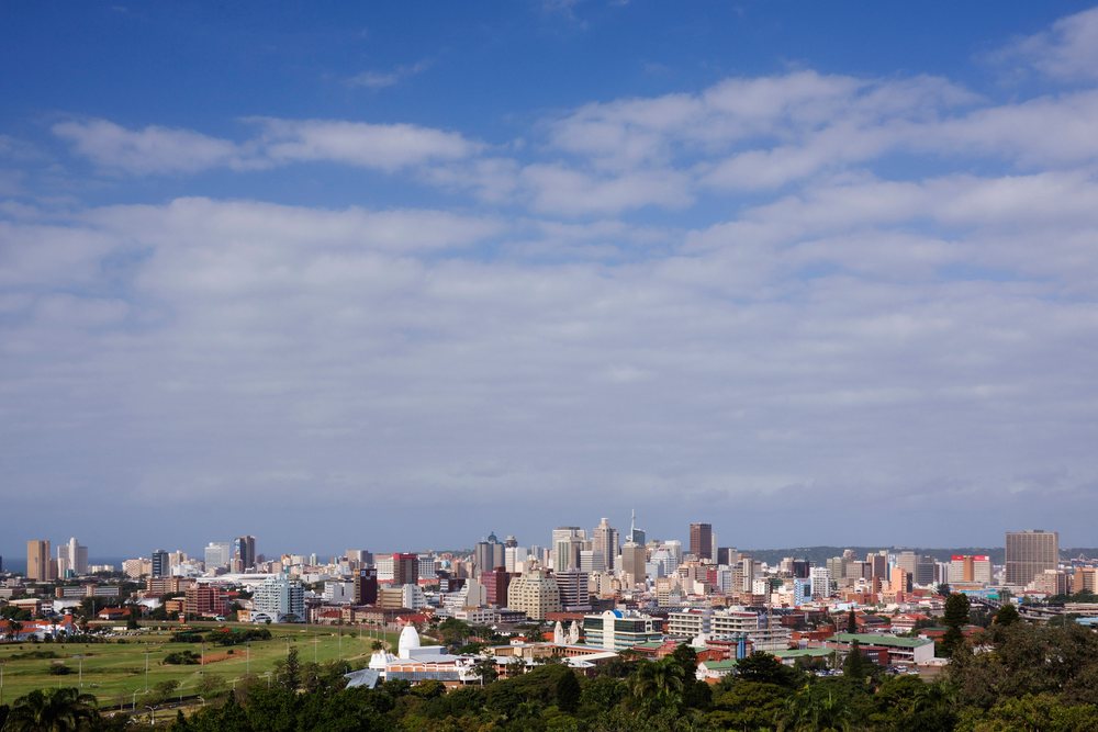 Durban city skyline viewed from Berea with green open space and Indian Ocean visible in the distance under a partly cloudy sky, KwaZulu Natal, South Africa.