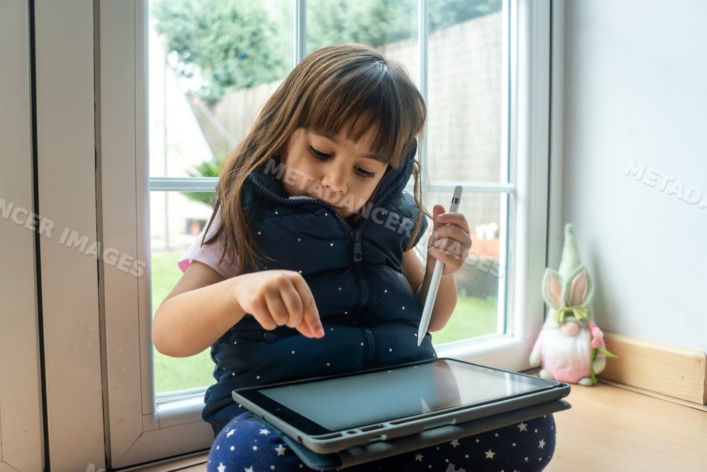 A young white girl uses a digital tablet with a stylus pen at home