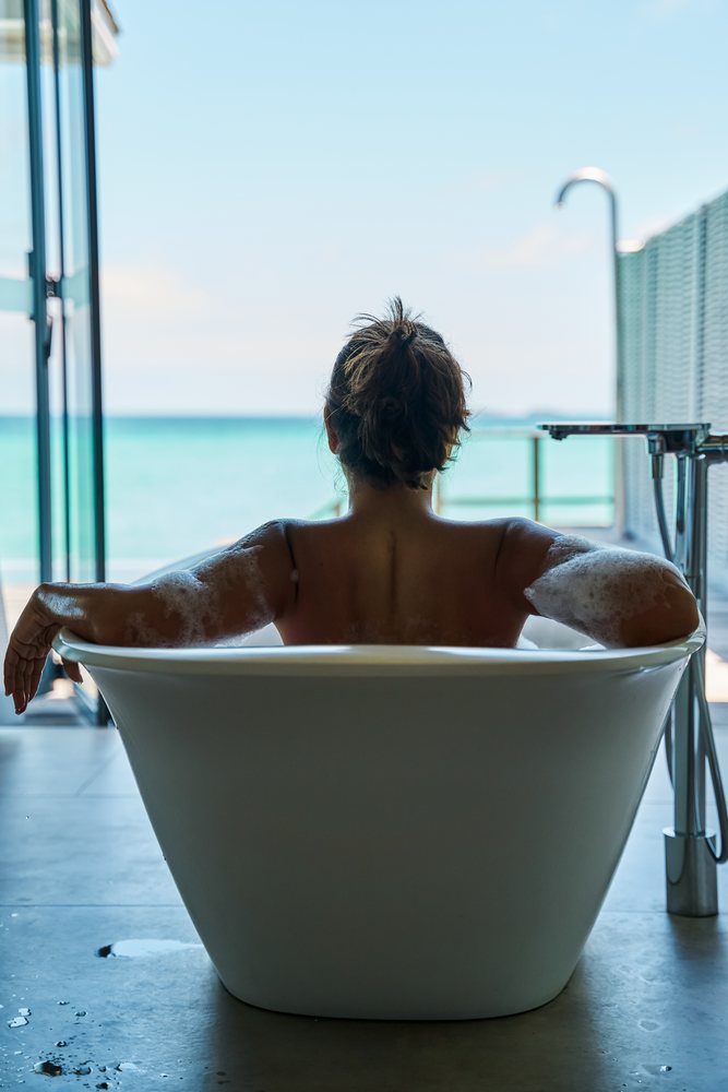 A woman is relaxing in a bubble bath in a modern bathtub with an ocean view in the, Maldives.