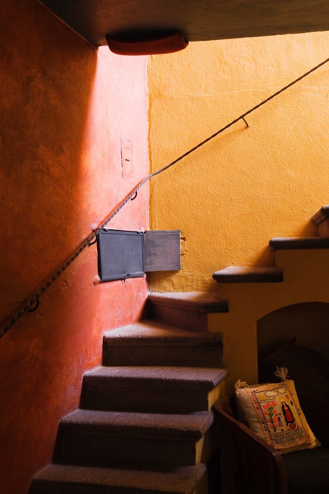 Rustic indoor stairway features textured orange and yellow walls beside a wood chair with a decorative pillow.