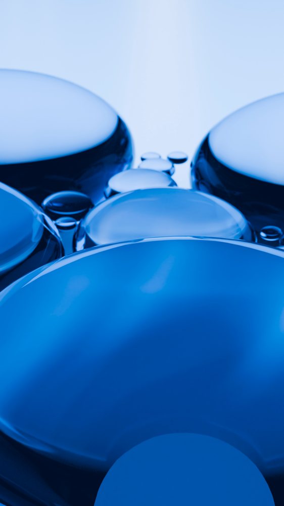 Macro close-up shows blue liquid droplets clustered on smooth surface highlighting surface tension and reflection.