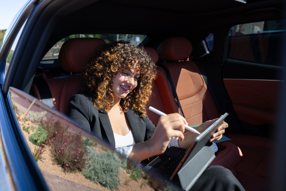 Businesswoman using a tablet with stylus inside a car with tan leather seats, remote work, Spain.