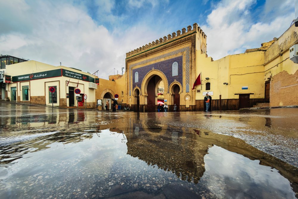 Flooded street near the Blue Gate (Bab Boujloud), shows reflections on wet pavement with people walking by under a cloudy sky, Landscape, Lifestyle, Fes, Fecs-Meknes Administrative Depar, Morocco.