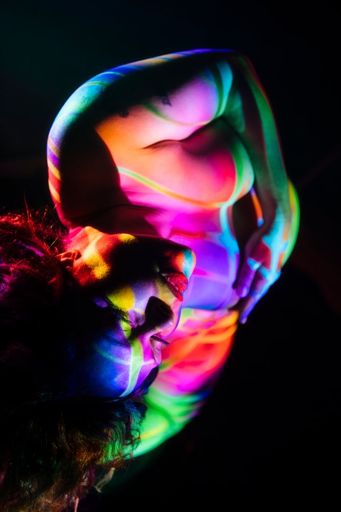 Pregnant woman with colorful light patterns projected on her nude body posing in a dark studio portrait, pregnancy.