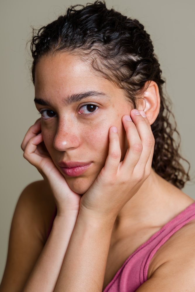 Close-up portrait of a woman with curly hair resting her face on her hands in a beauty shoot studio, Spain.