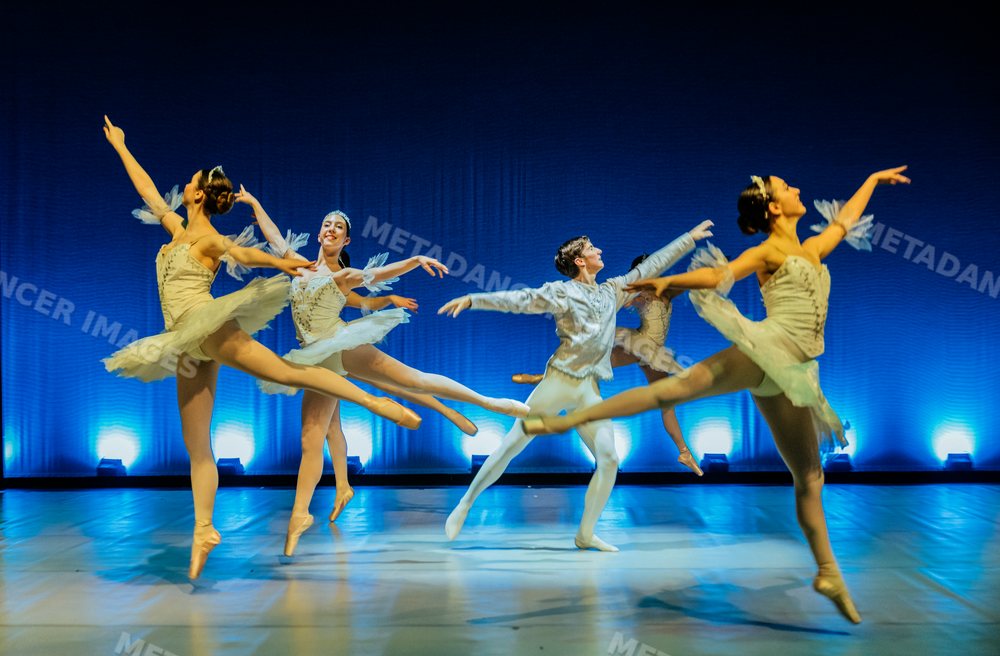 Ballet dancers perform a leap on stage in a holiday-themed ballet
