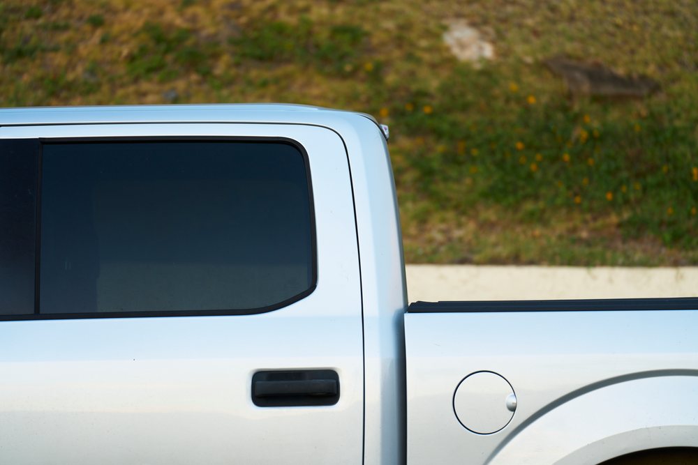 Silver pickup truck side door, window, and fuel cap visible outdoors on grass, Oahu, Hawaii, USA.