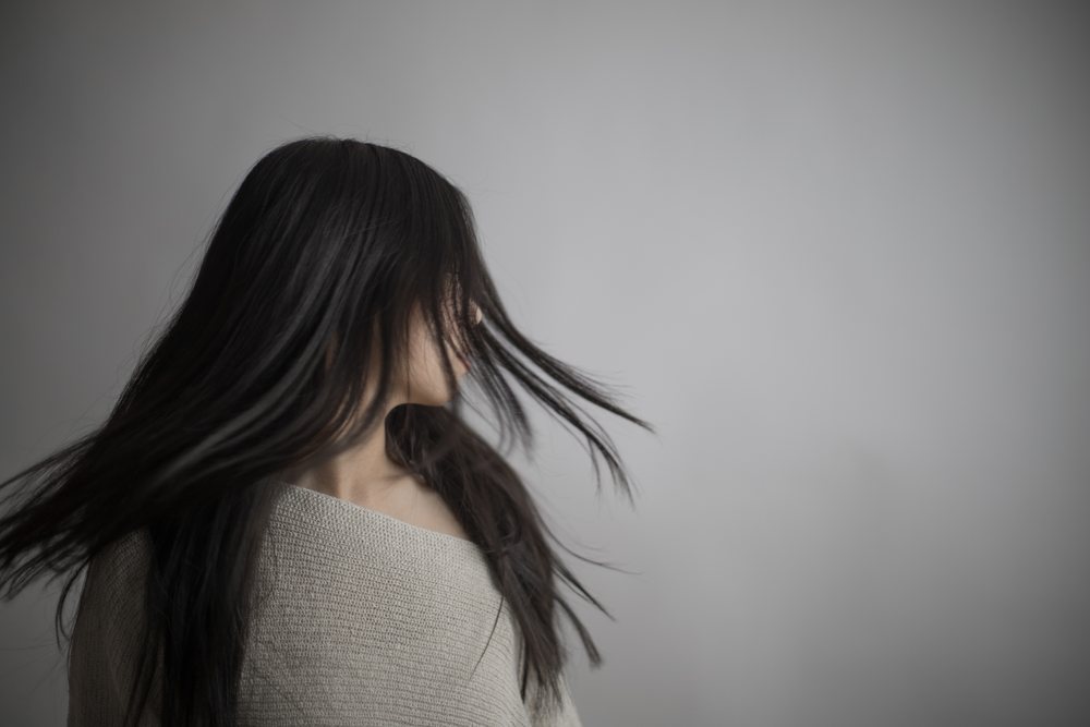 Young woman with long black hair turning her head sideways in motion against a neutral gray background in studio lighting, Art, portrait, emotional.