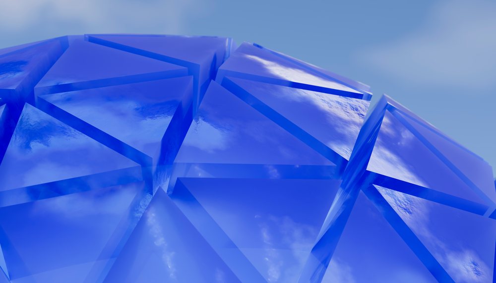 Blue transparent glass triangular shapes forming a fragmented geometric pattern with reflections of the sky on the smooth surfaces.