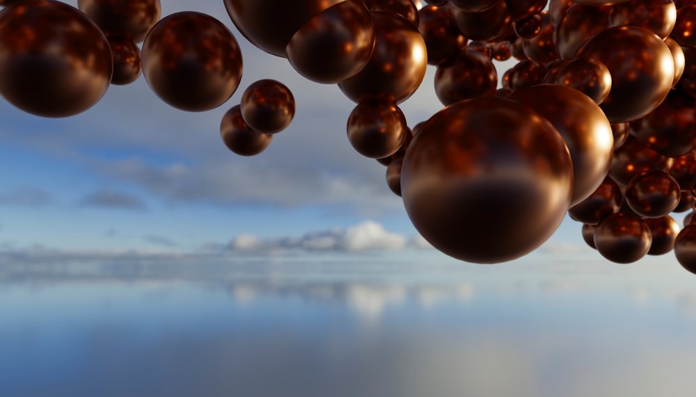 A cluster of reflective brown spheres floating over calm water with soft cloud reflections and a blue sky background.
