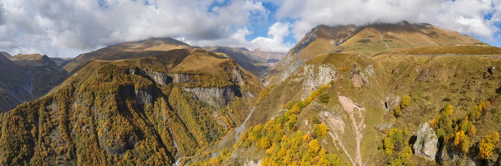 Autumn foliage colors the Sherkhota Mountain and Southern Caucasus range under a partly cloudy sky, Gudauri, Mtiuleti Region, Georgia.