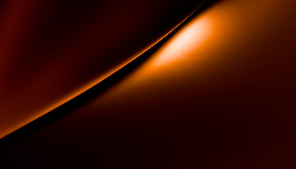 Abstract composition of curved orange light and shadow forming a smooth glowing surface with dynamic contrast.