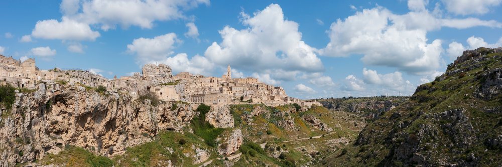 Skyline of Matera on the edge of the Gravina River Gorge with ancient buildings and cliffs under a blue sky, Basilicata, Italy.