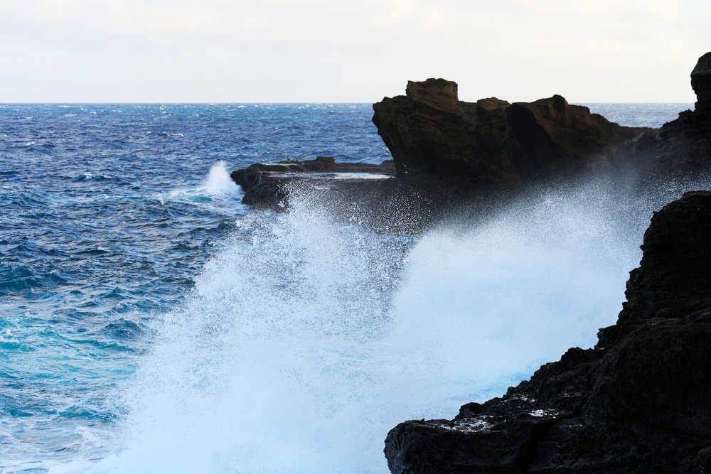 Waves crash against the rocky coastline, creating water spray over the ocean shore, Oahu, Hawaii, USA.