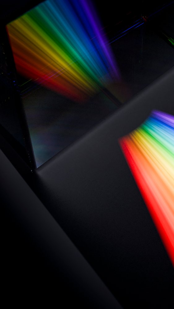 Prism reflects a colorful rainbow light spectrum onto a dark surface.