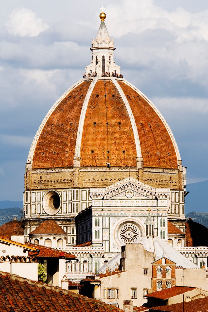 Santa Maria del Fiore cathedral dome with tourists on observation deck overlooks Florence city under a cloudy blue sky, Italy.