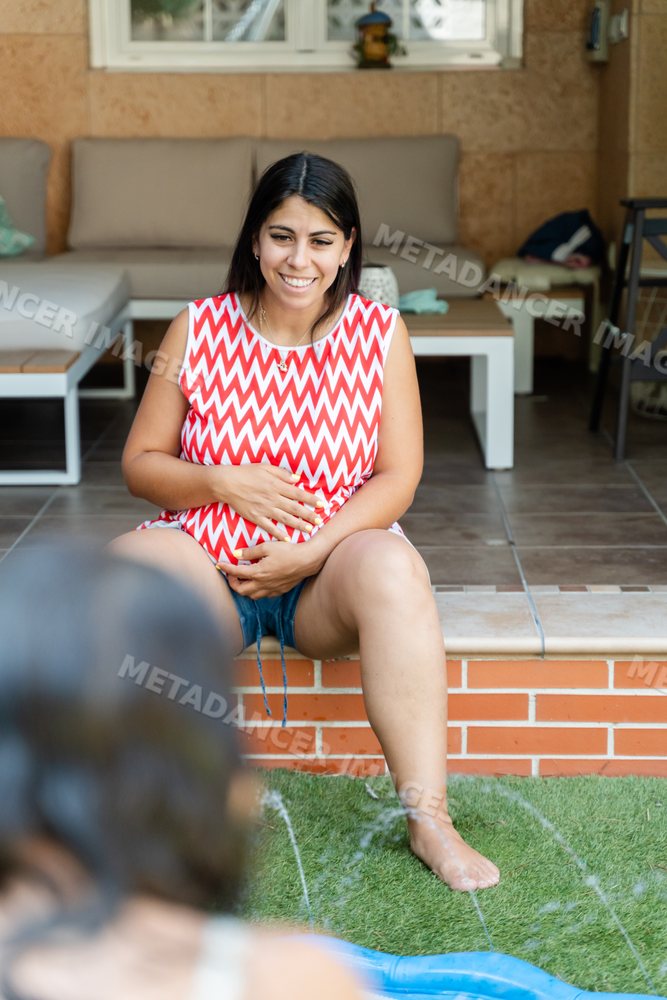 Pregnant white woman sitting outdoors holding her belly in a backyard