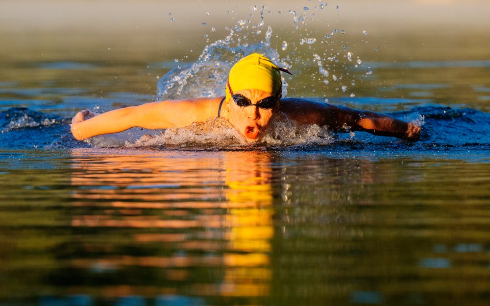 Swimmer performing butterfly stroke in open water wearing a yellow swim cap and goggles, USA.