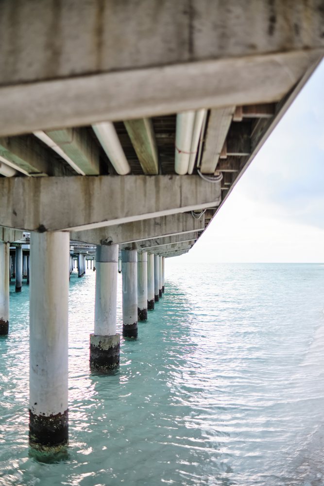 View underneath a concrete pier with pillars in turquoise ocean water