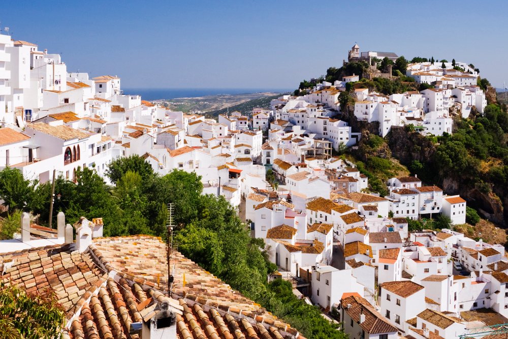 Hilltop village with whitewashed buildings, terracotta rooftops, and a historic stone fortress overlooking the Mediterranean Sea, Andalucia, Spain.