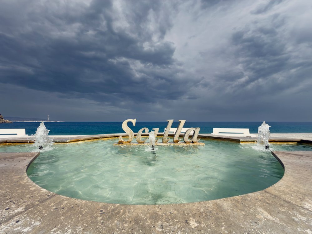 Fountain with white 'Scilla' letters by the sea under a stormy sky on the Calabria coast, Italy.