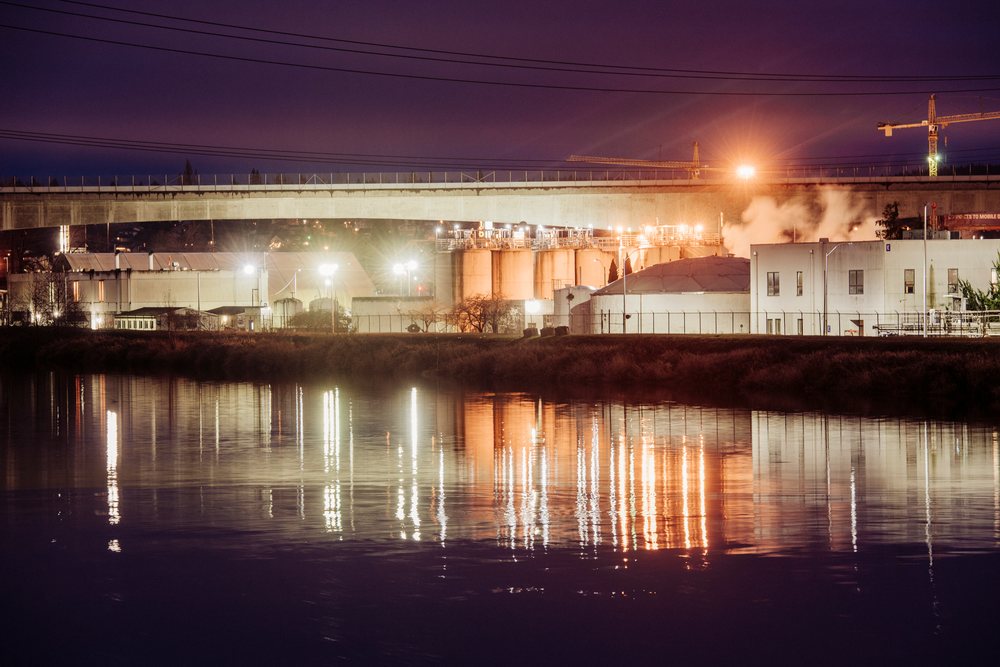 Industrial complex with illuminated buildings, concrete bridge, and steam rising over water at night in an urban environment, Tacoma, WA, USA.
