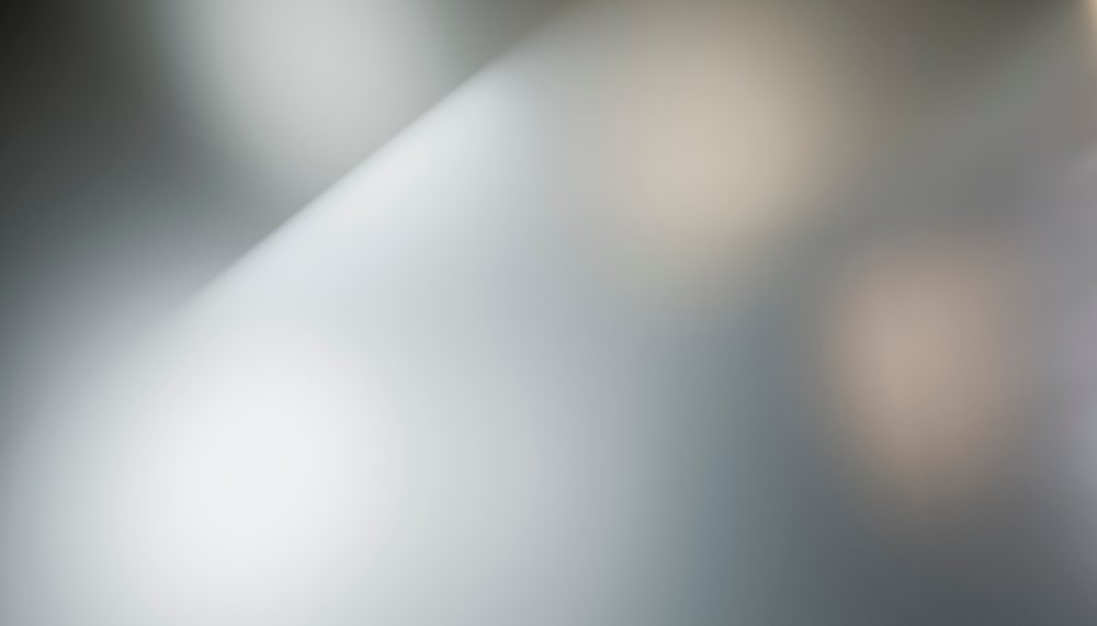 Abstract blurred background featuring soft light and neutral gray gradient tones with subtle bokeh effect.