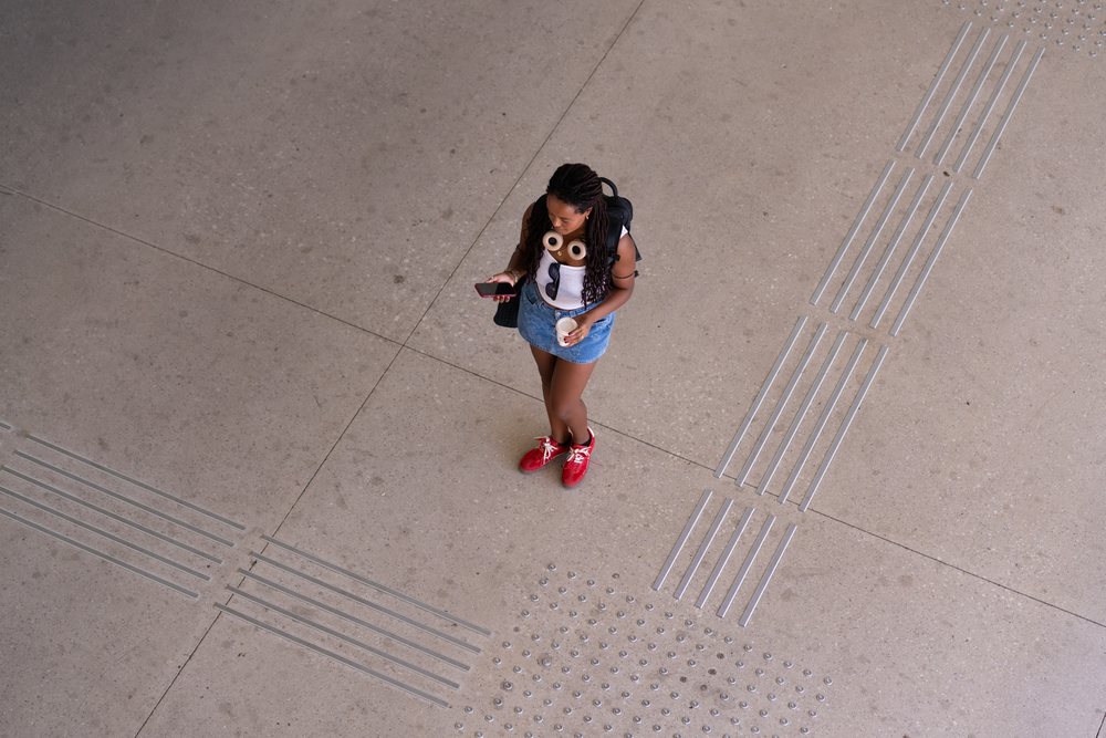 Woman standing on tactile paving holding a cup and looking at her phone, travel, Santiago De Compostela, Spain.