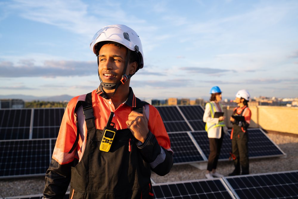 Solar technician in safety gear communicates with team members on a rooftop with solar panels at sunset, Madrid, Spain.