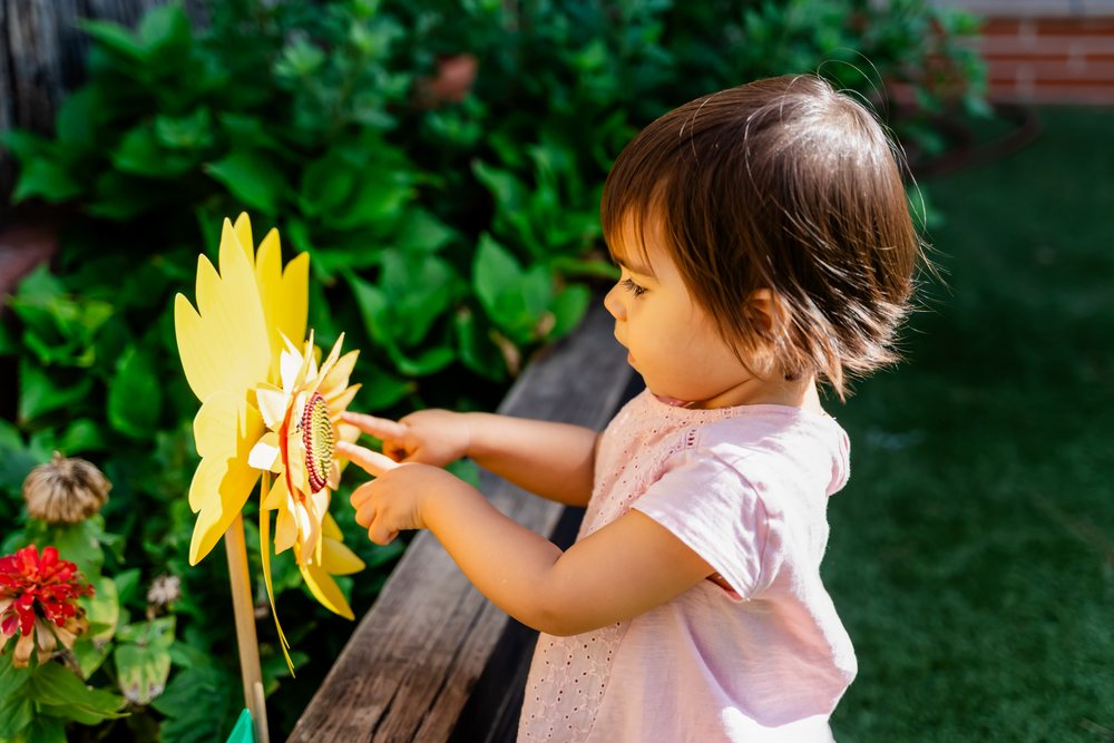 Toddler girl touching a yellow sunflower decoration on a wooden plank in a garden in Spain during daylight, kids.