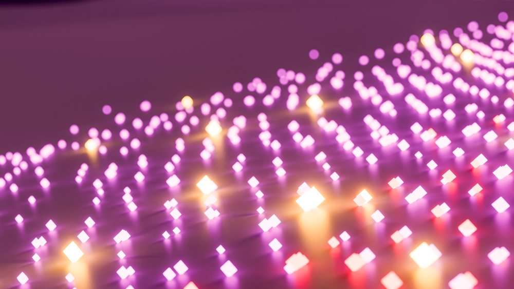 Glowing purple and yellow lights arranged in rows form an abstract digital pattern with bokeh illumination on a dark background.