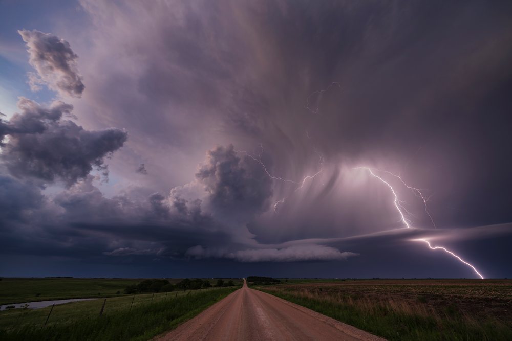 Supercell thunderstorm with multiple Lightning strikes over a rural dirt road and fields at Sunset, Storm Chasing, Weather, Environmental, Jansen, Nebraska, USA.