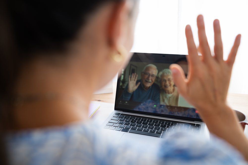 Elderly couple waving during a video call on a laptop in a home office setting, telecommuting, Spain.