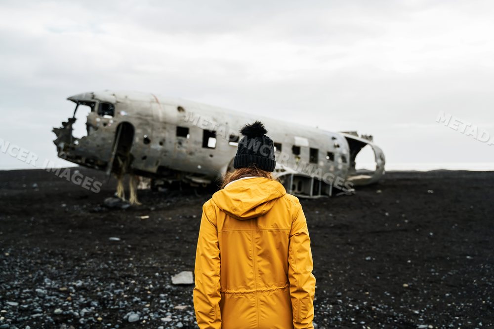 A white woman in a yellow jacket explores a wrecked airplane
