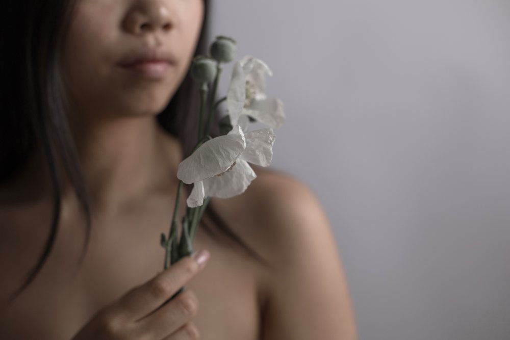 Woman holds a white flower near her face with an emotional expression against a soft gray background, Art, portrait.