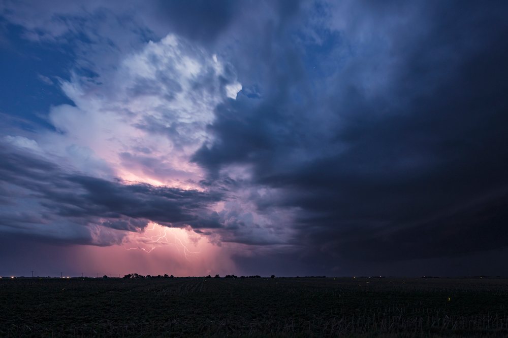 Lightning bolts illuminate dark Storm clouds over an open farmland in the Great Plains at twilight, Wilcox, Nebraska, USA.