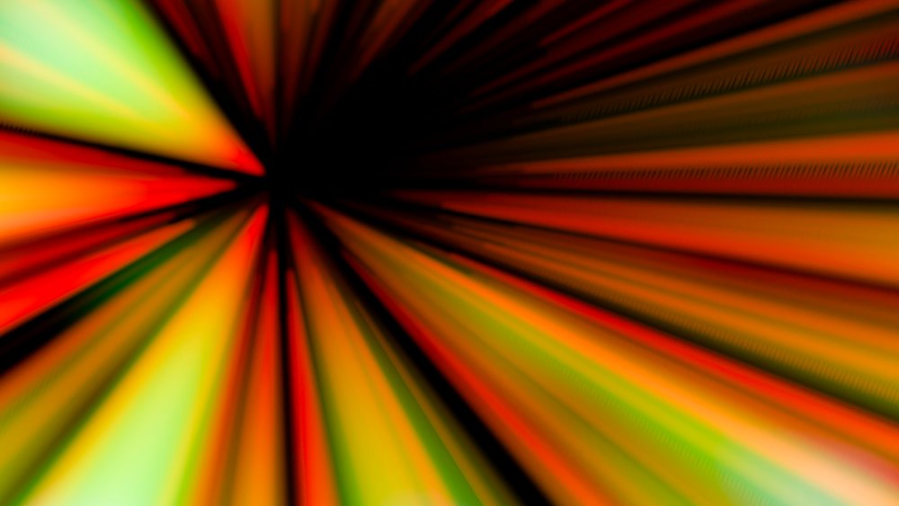 Colorful radial lines in orange, red, yellow, and green emerge from a black center with a motion blur effect creating a vibrant dynamic background.