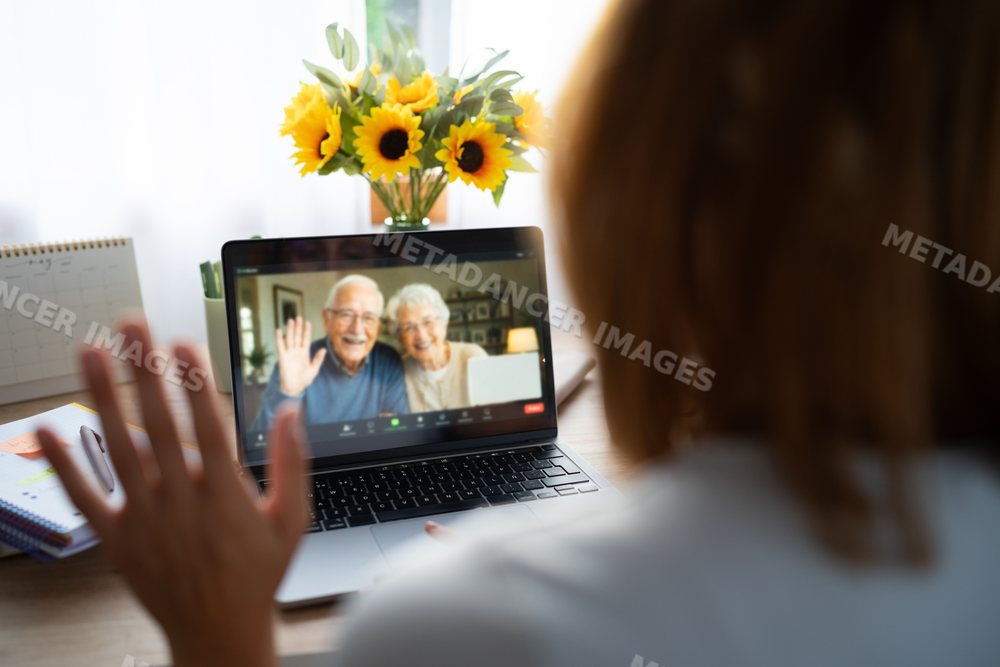 A white woman waves at a senior couple during a video call at home