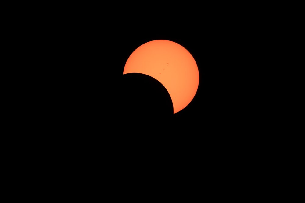 Solar eclipse with the moon partially covering the sun, showing sunspots and a dark silhouette against the sky over, Los Angeles, USA.