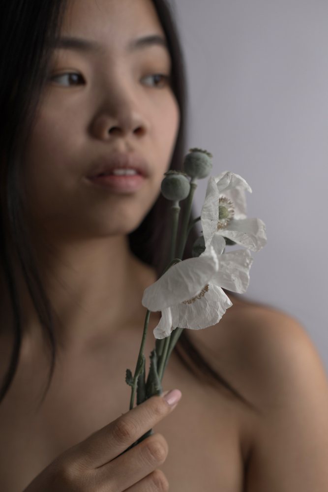 Close-up indoor portrait of a woman holding white flowers with poppy seed heads under soft lighting, Art, emotional.