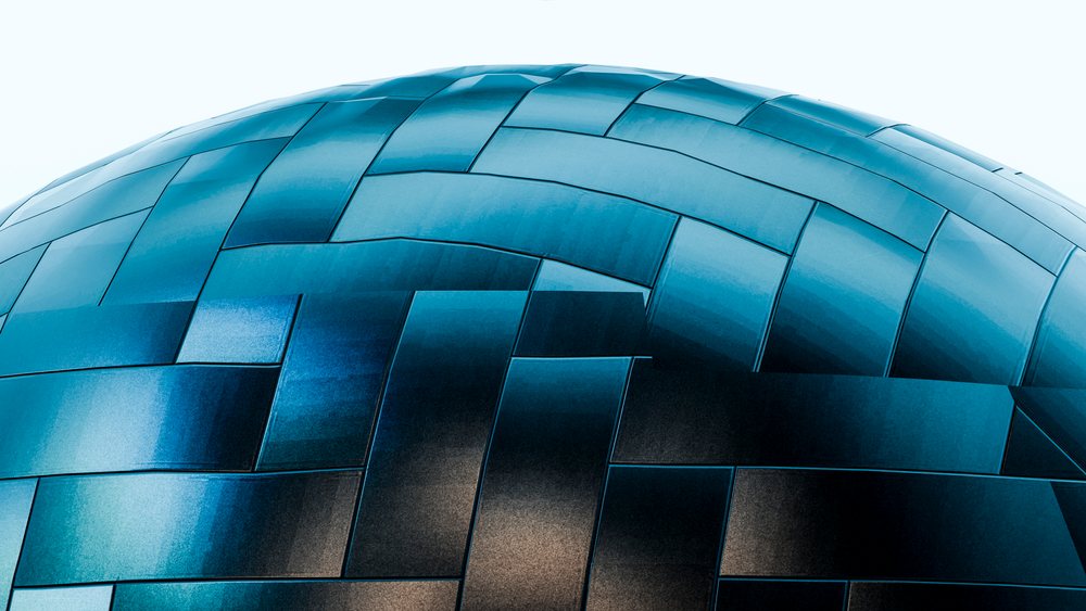 Curved metal architecture with blue reflective panels forming a geometric pattern on a modern building exterior.