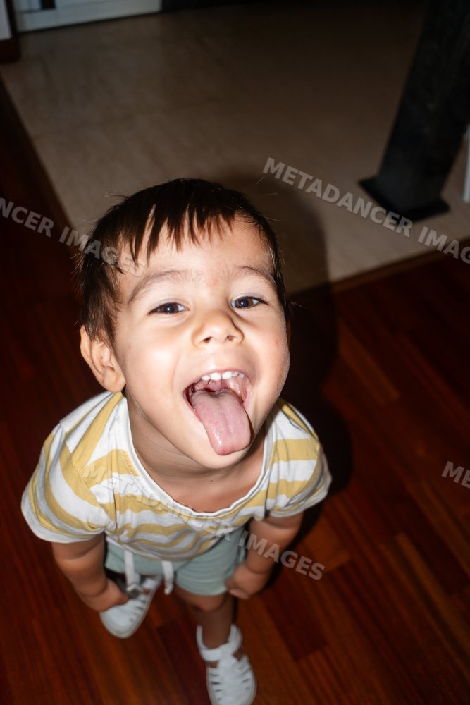 A young white boy playfully sticks out his tongue indoors on wood