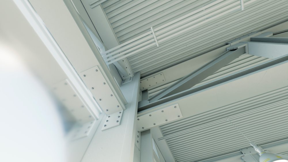 Metal beams and steel framework form the industrial warehouse ceiling inside a manufacturing plant with visible lighting fixtures, car, industry.