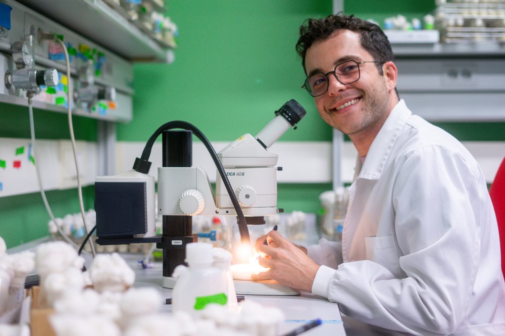 A smiling scientist wearing a white lab coat uses a microscope, science, biology, research, Inside A Research Laboratory.