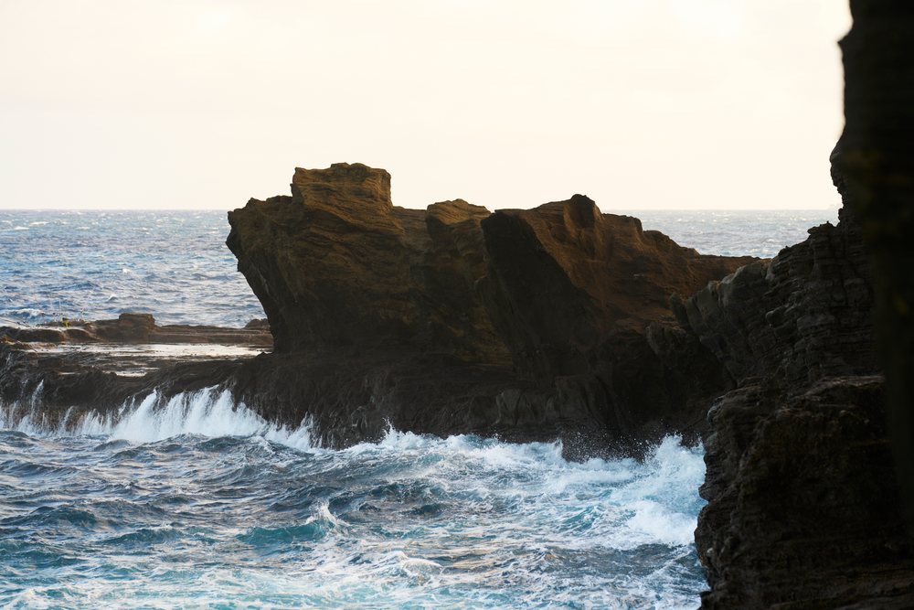 Ocean waves crash against cliff rocks along a rocky coastline during daylight, Oahu, Hawaii, USA.