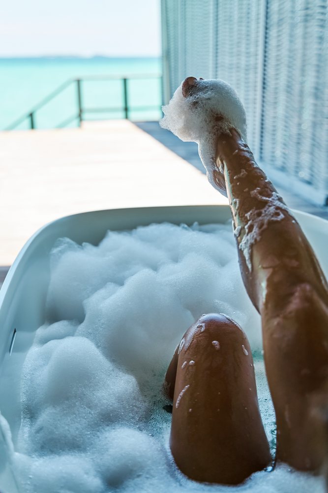 A person enjoys a bubble bath with soapy foam on their leg at a bathtub with a view in the, Maldives.